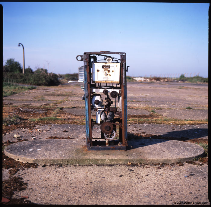 Orford Ness - An aging petrol pump stands alone, surrounded by piles of debris